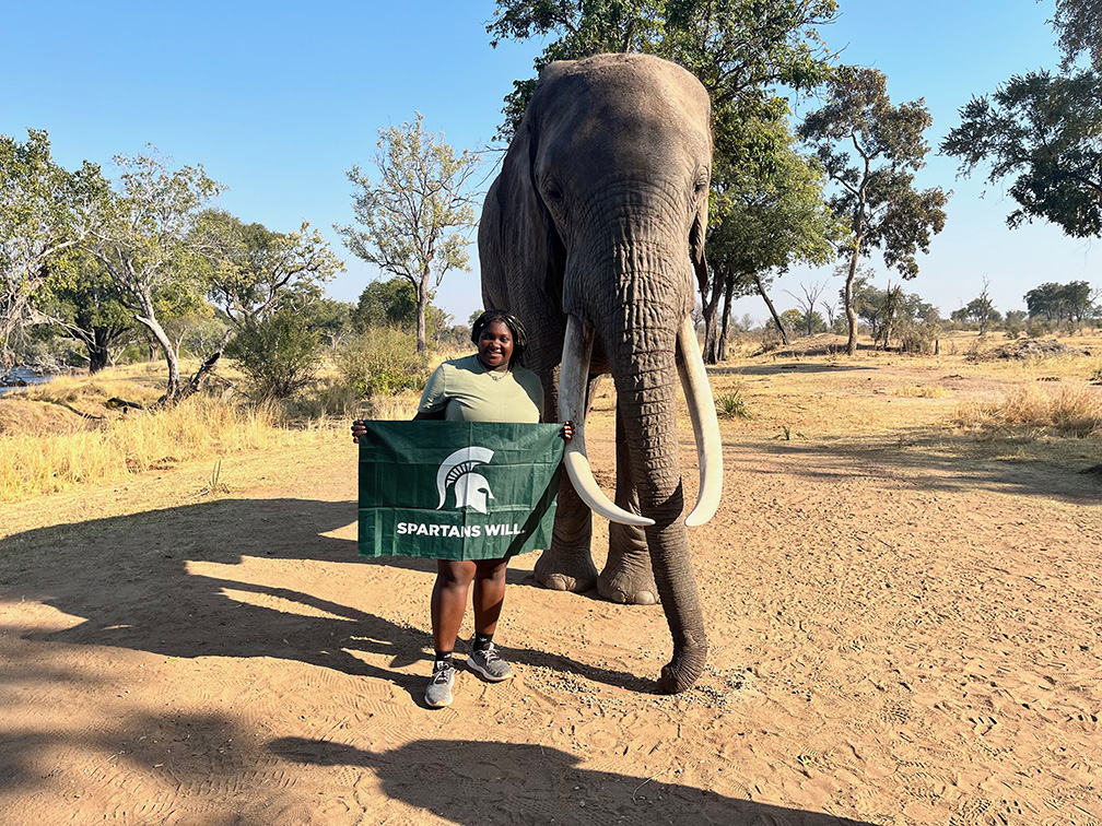 Student holding Spartans Will flag next to an elephant