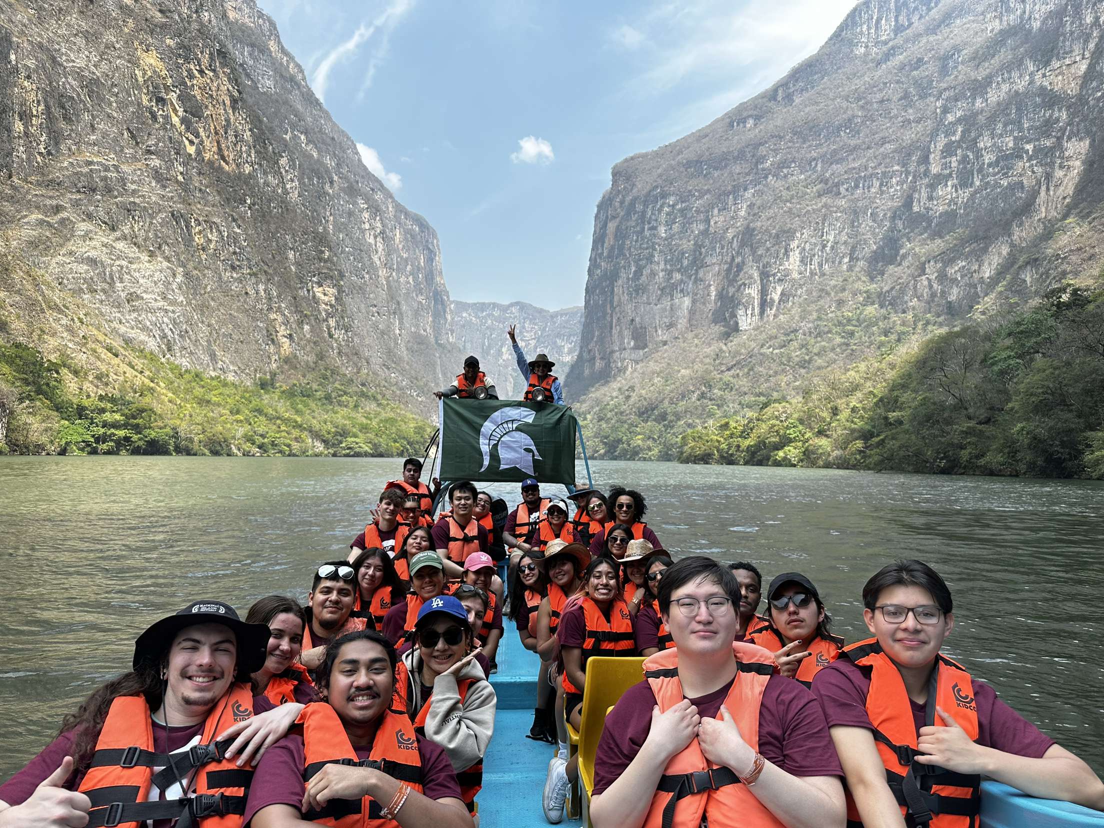 Group of students on a raft on a river with mountains in the background